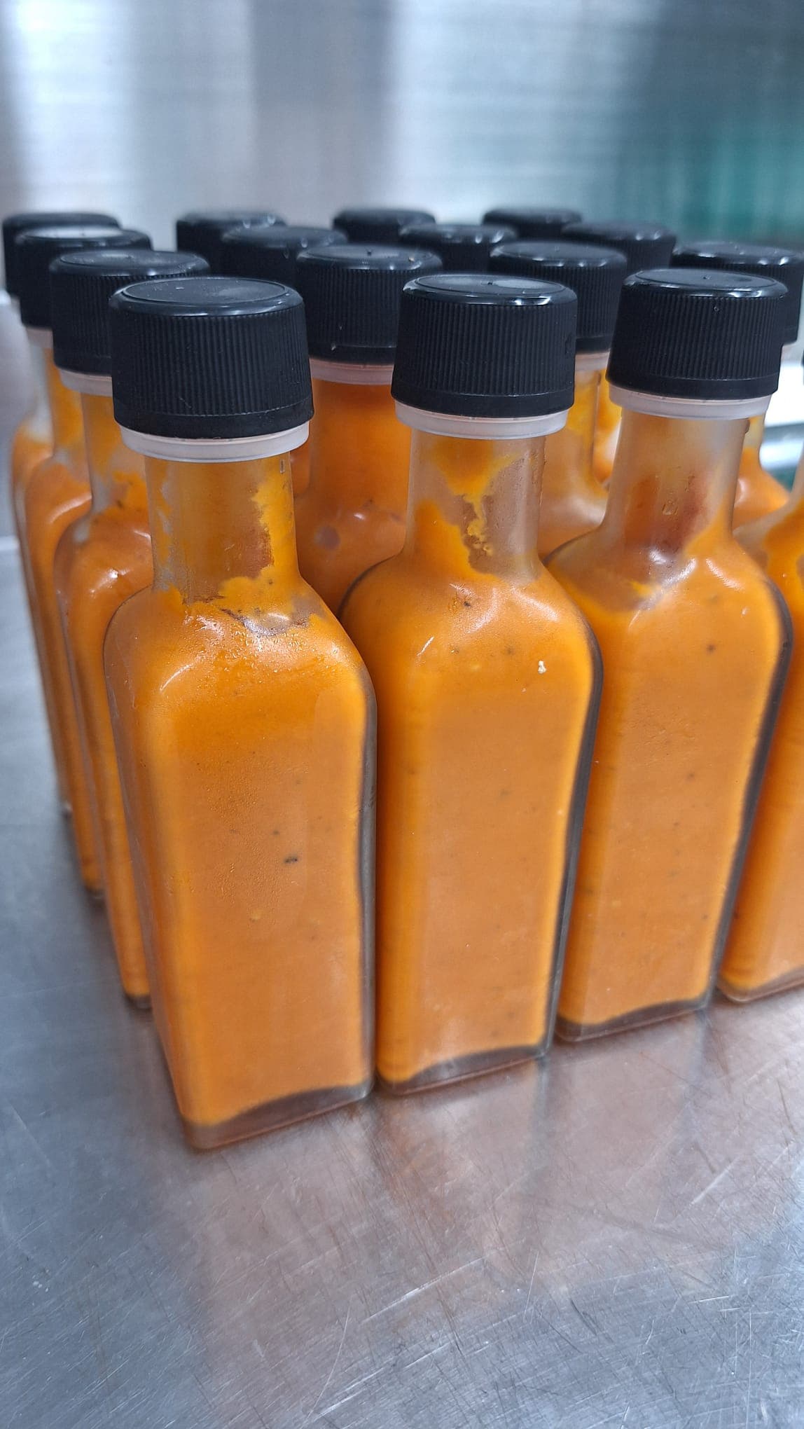 Rows of freshly bottled Mama Amaya's sauce, capped and ready — placeholder pending a real photo of all four sauces together