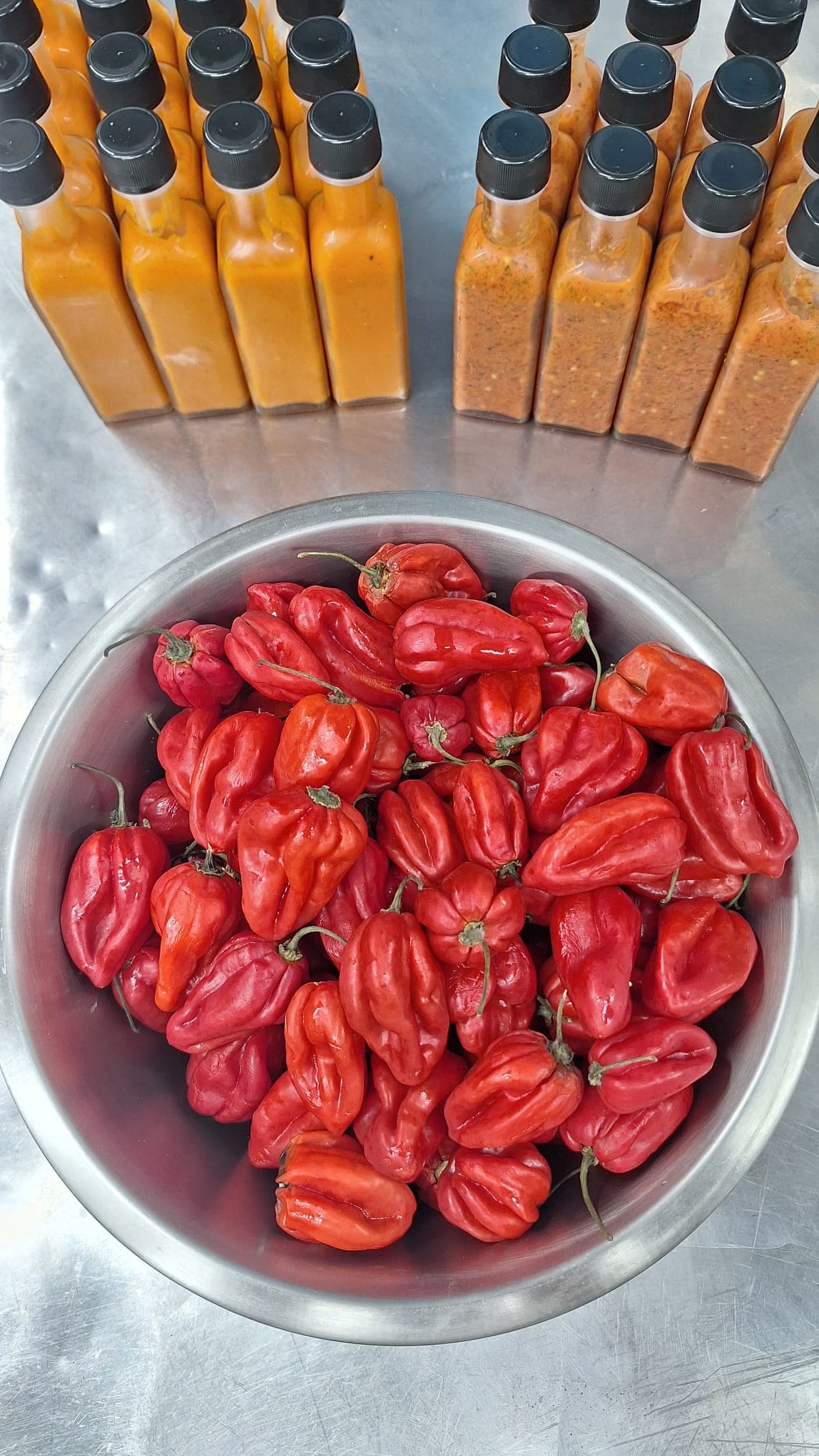 A bowl of fresh red habanero chillies with bottled sauce blurred in the background